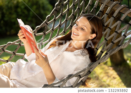 Young woman lying in hammock, reading a book and looking contented 132293892