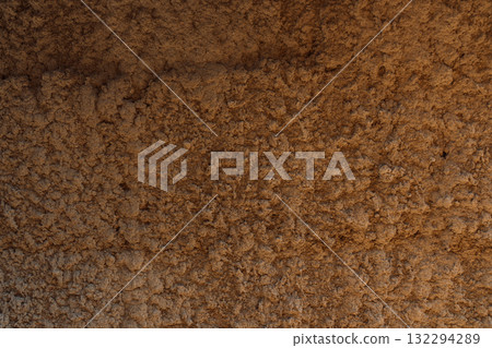 Rough brown earthen wall rammed earth or clay plaster with horizontal banding and irregular granules. Natural architectural background. Rough brown earthen wall rammed earth or clay plaster with horizontal banding and irregular granules. Natural architectural background. 132294289