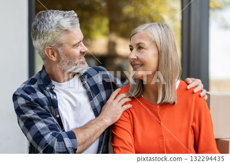 Happy senior couple sitting outside home near moving boxes Happy senior couple sitting outside home near moving boxes 132294435