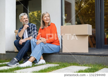 Mature couple resting on porch next to packed boxes after relocation Mature couple resting on porch next to packed boxes after relocation 132294440