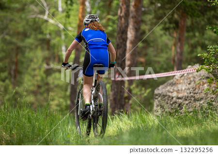Rear view woman riding mountain bike in forest next to large rock Rear view woman riding mountain bike in forest next to large rock 132295256