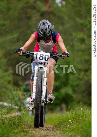 Female athlete riding bowed head on mountain bike in forest race 132295259