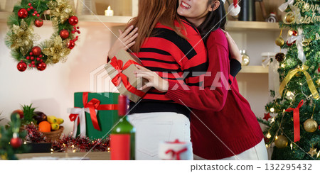 Christmas Celebration. Two friends embracing with gifts in a festive kitchen. 132295432