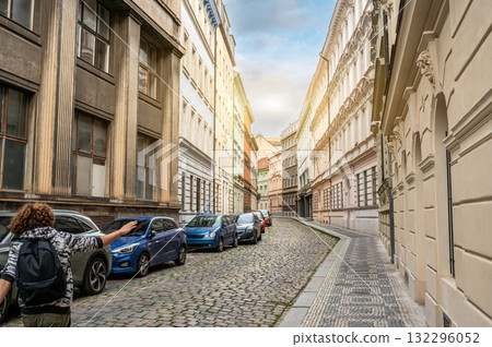 Prague, Czech Republic, August 7, 2023. Street photography exploring the old town: a young man with curly hair and a backpack points the way past the colorful period buildings. Travel destinations. 132296052
