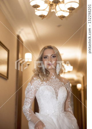 close up of beautiful blonde bride in long white dress in hotel hallway 132298201