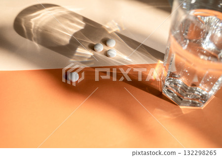 pills and glass of water on orange background with sun rays pills and glass of water on orange background with sun rays 132298265