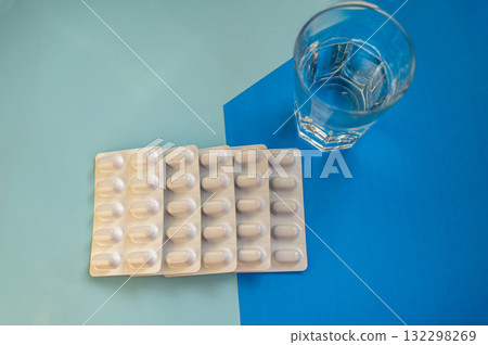 Medical pills in a blister and a glass of water on a blue background Medical pills in a blister and a glass of water on a blue background 132298269