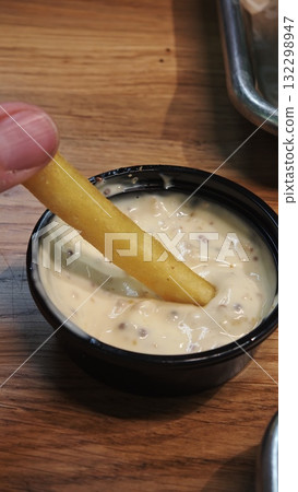 Close-up of a French fry dipped in creamy mustard sauce on a wooden table Close-up of a French fry dipped in creamy mustard sauce on a wooden table 132298947