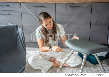 Young woman sitting on the floor assembling a chair with tools. Concept of female independence and do it yourself lifestyle. Young woman sitting on the floor assembling a chair with tools. Concept of female independence and do it yourself lifestyle. 132299358