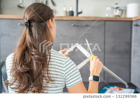 Young woman seen from behind assembling a chair with screwdrivers on the floor at home. Feminist concept of female independence and do it yourself furniture assembly. 132299366