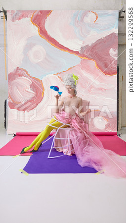 Elegant woman in Marie Antoinette character holding blue cocktail with feather garnish on abstract background. Elegant woman in Marie Antoinette character holding blue cocktail with feather garnish on abstract background. 132299568