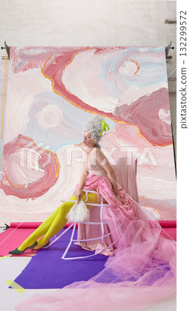 Graceful rococo woman sitting in pink gown with fan on abstract backdrop Graceful rococo woman sitting in pink gown with fan on abstract backdrop 132299572