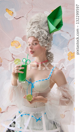 Elegant woman dressed as Marie Antoinette holding green cocktail with lime slices and soft smile. Elegant woman dressed as Marie Antoinette holding green cocktail with lime slices and soft smile. 132299597