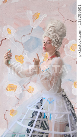 Playful rococo woman making selfie gesture with smartphone in floral studio Playful rococo woman making selfie gesture with smartphone in floral studio 132299601