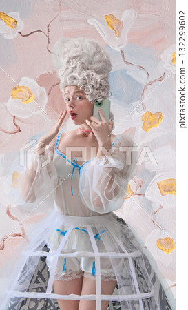 Surprised woman dressed as Marie Antoinette talking on smartphone against painted floral wall. 132299602
