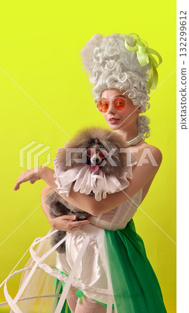 Stylish rococo woman with sunglasses holding fashionable poodle on yellow background Stylish rococo woman with sunglasses holding fashionable poodle on yellow background 132299612