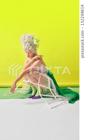 Rococo woman in green and white Marie Antoinette costume crouching on yellow background 132299614