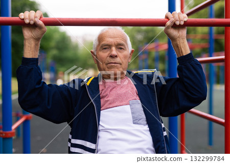 Elderly man pulls himself up on a horizontal bar on street sports field 132299784
