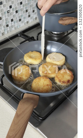 Anonymous person fries potato croquettes in vegetable oil in new, trendy frying pan. Farm produce. Home cooking. Traditional cuisine. Anonymous person fries potato croquettes in vegetable oil in new, trendy frying pan. Farm produce. Home cooking. Traditional cuisine. 132300820