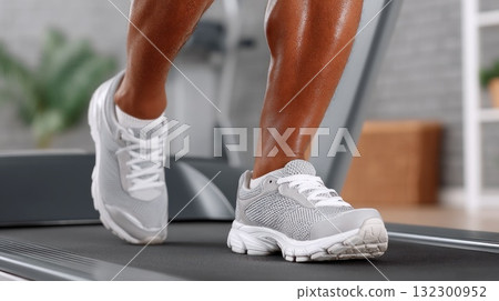 A person is exercising on a treadmill in a well lit home gym with athletic shoes 132300952
