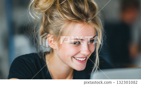 Bright and cheerful young woman engages with her laptop smiling in a lively workspace atmosphere 132301082