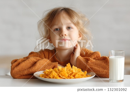 A girl sits at the table looking content as she enjoys cereal and a glass of milk during breakfast 132301092