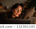Woman with headphones appears thoughtful while watching something on her laptop in intimate lighting 132301185