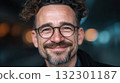 Smiling man with curly hair and glasses stands in a contemporary indoor area showcasing a joyful demeanor 132301187