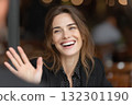 Woman with long hair smiles and waves while enjoying time with friends at a lively cafe 132301190
