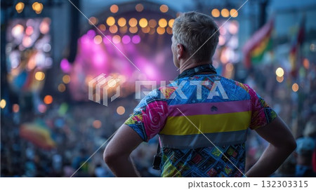 Man with back to camera, wearing a vibrant patterned shirt, enjoys a lively music concert with a blurred stage and lights 132303315