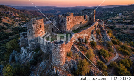 Ancient medieval castle ruins perched on rocky hilltop during golden sunset with rolling countryside landscape stretching into distance Ancient medieval castle ruins perched on rocky hilltop during golden sunset with rolling countryside landscape stretching into distance 132303320
