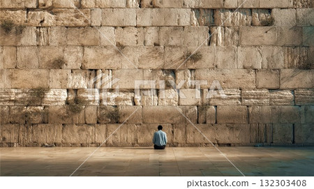 Solitary person sitting in contemplation before massive ancient stone wall, showcasing scale and historical architecture in peaceful moment 132303408