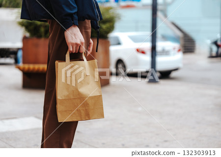 Individual holding a brown paper bag while standing on a city street in daytime Individual holding a brown paper bag while standing on a city street in daytime 132303913