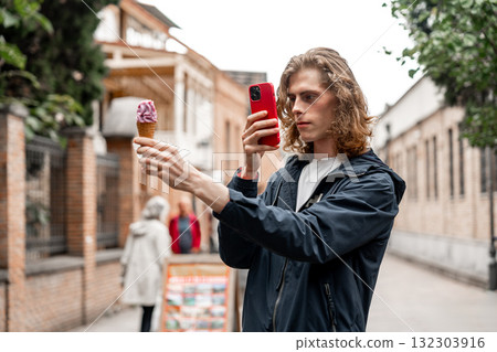 Boy enjoying ice cream while taking a selfie on a city street during daytime 132303916