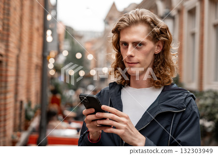 Young man checking phone in bustling city alley lit by string lights Young man checking phone in bustling city alley lit by string lights 132303949