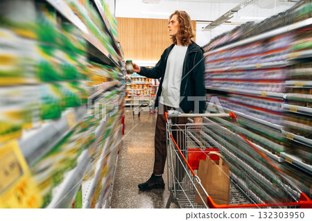 Young man shopping for groceries in a supermarket aisle during daytime Young man shopping for groceries in a supermarket aisle during daytime 132303950
