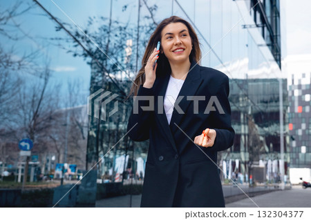 Business Professional on Phone Strolls Past Modern Glass Building in Urban Setting During Sunny Morning Business Professional on Phone Strolls Past Modern Glass Building in Urban Setting During Sunny Morning 132304377