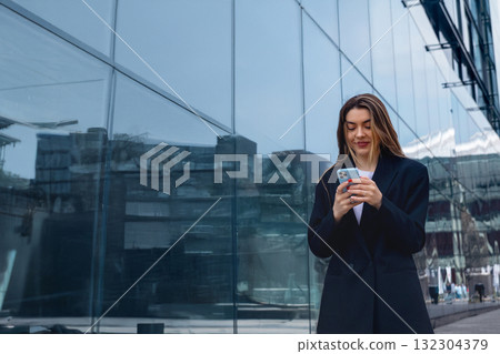 Woman in Formal Attire Checks Phone Outside Modern Building During Daytime in Urban Setting Woman in Formal Attire Checks Phone Outside Modern Building During Daytime in Urban Setting 132304379