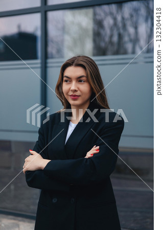Confident Woman in a Black Blazer Standing Outside a Modern Building During Twilight 132304418