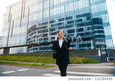 Confident Businesswoman Walking Along the City Sidewalk in Front of a Modern Glass Building During a Sunny Day 132304429