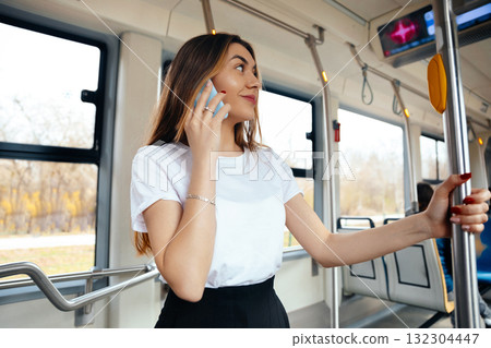 Young Woman on Public Transport Talking on Phone While Standing in a Modern Tram During Daylight Hours Young Woman on Public Transport Talking on Phone While Standing in a Modern Tram During Daylight Hours 132304447