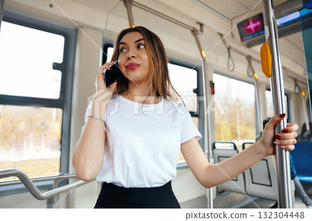 Young Woman Talking on Mobile Phone While Standing in Public Transportation During Daytime in Urban Setting Young Woman Talking on Mobile Phone While Standing in Public Transportation During Daytime in Urban Setting 132304448