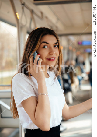 Young Woman Talking on Phone in Public Transportation During Daytime, Surrounded by Commuters and City Views Outside Young Woman Talking on Phone in Public Transportation During Daytime, Surrounded by Commuters and City Views Outside 132304449