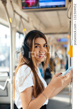 Young Woman Enjoys Music on Public Transport While Checking Her Phone During the Morning Commute in a Vibrant City Setting 132304452