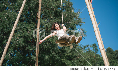 Joyful child swinging on a wooden swing in a sunny outdoor park surrounded by green trees with blue sky above, capturing happiness and freedom 132304775