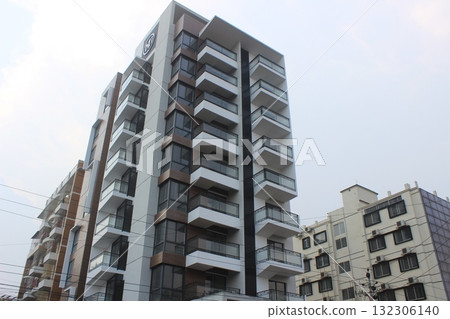 Modern residential building with multiple balconies and a contemporary facade, viewed from a low angle against a bright sky Modern residential building with multiple balconies and a contemporary facade, viewed from a low angle against a bright sky 132306140
