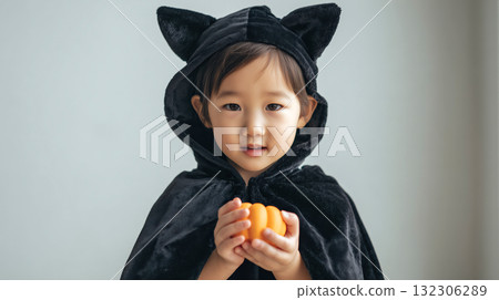 A toddler dressed as a cat indoors holds an orange autumn pumpkin 132306289