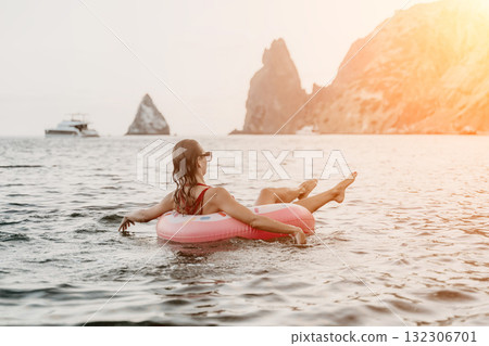 Woman, Ocean, Relaxing. Woman floats on pink ring in ocean by rocky cliffs at sunset, generous copy space. Woman, Ocean, Relaxing. Woman floats on pink ring in ocean by rocky cliffs at sunset, generous copy space. 132306701