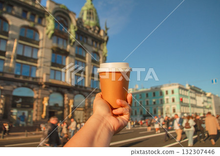 Paper cup of natural coffee in women's hand against backdrop of Singer House on Nevsky Prospekt in center of St. Petersburg, Russia Paper cup of natural coffee in women's hand against backdrop of Singer House on Nevsky Prospekt in center of St. Petersburg, Russia 132307446