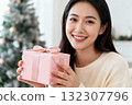 聖誕樹前拿著粉紅色禮物微笑的女人 132307796